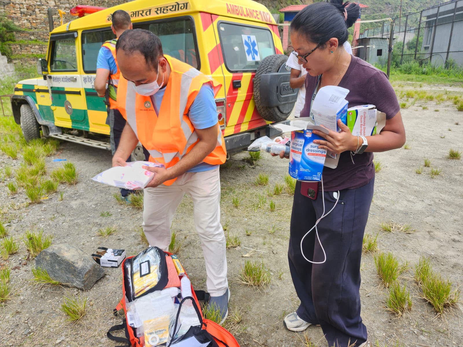 Hospital staff sorting patient care supplies beside an ambulance in a rural setting.