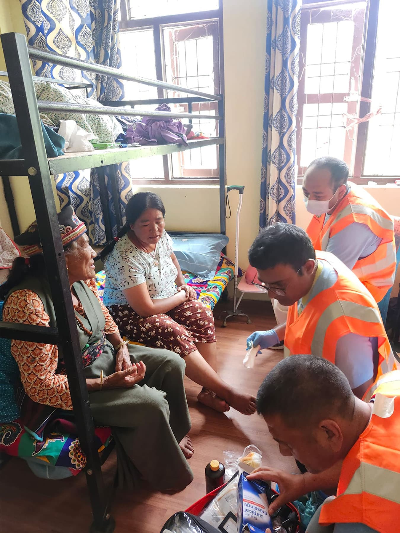 A responder in an orange vest checking on evacuees seated together in a shelter.