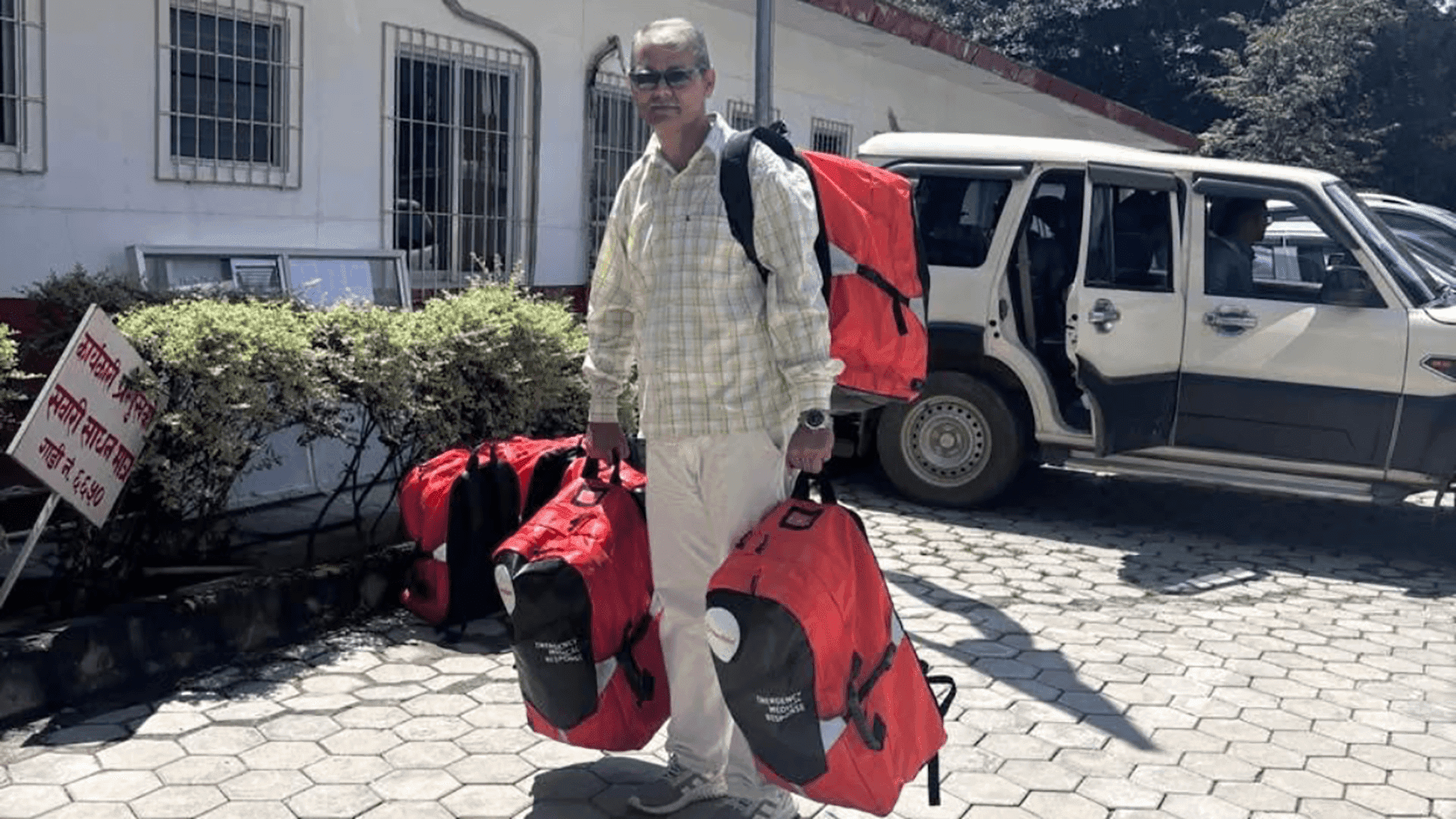 A field worker standing beside a vehicle with red emergency duffel bags.