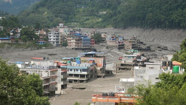 Aerial view of a riverside town buried under flood debris with damaged buildings.