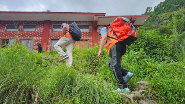 Responders hiking uphill through tall grass carrying red backpacks.