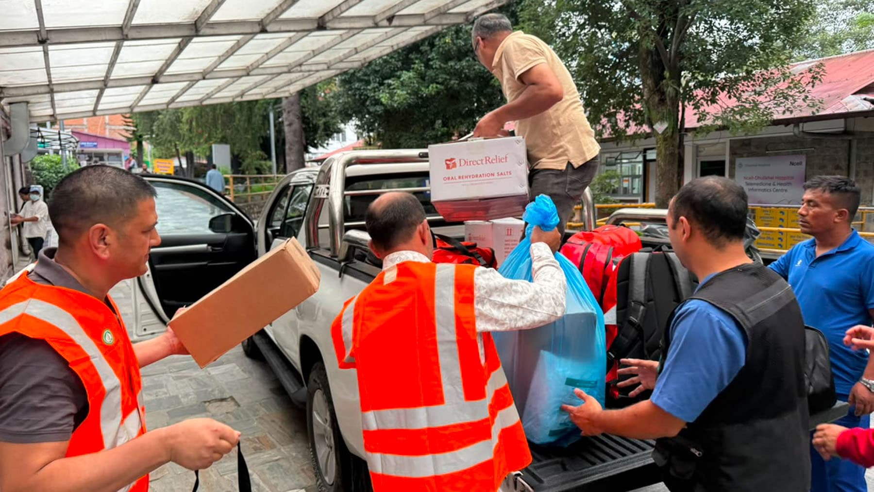 Volunteers in orange safety vests loading supply boxes into the back of a pickup truck.